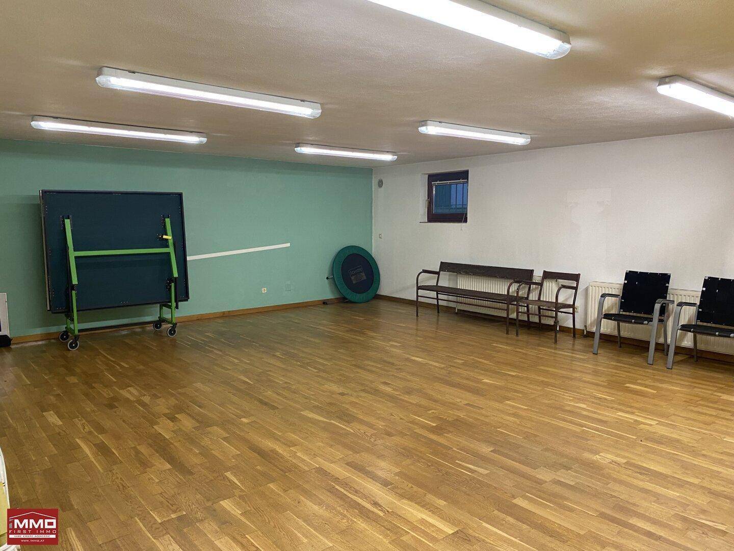 Vielseitiger Raum mit Holzboden und Tischtennisplatte, geeignet für verschiedene Aktivitäten.