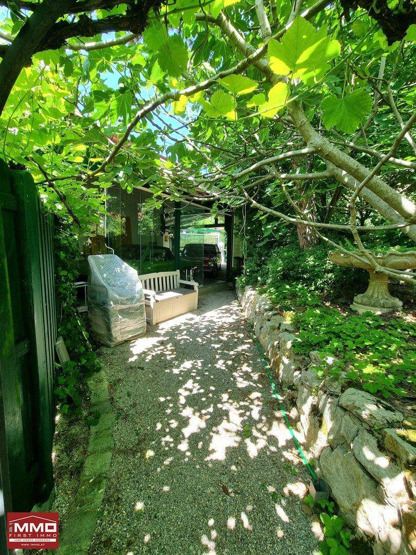 Grüner Gartenweg unter einer Pergola mit üppiger Vegetation und versteckten Sitzgelegenheiten.