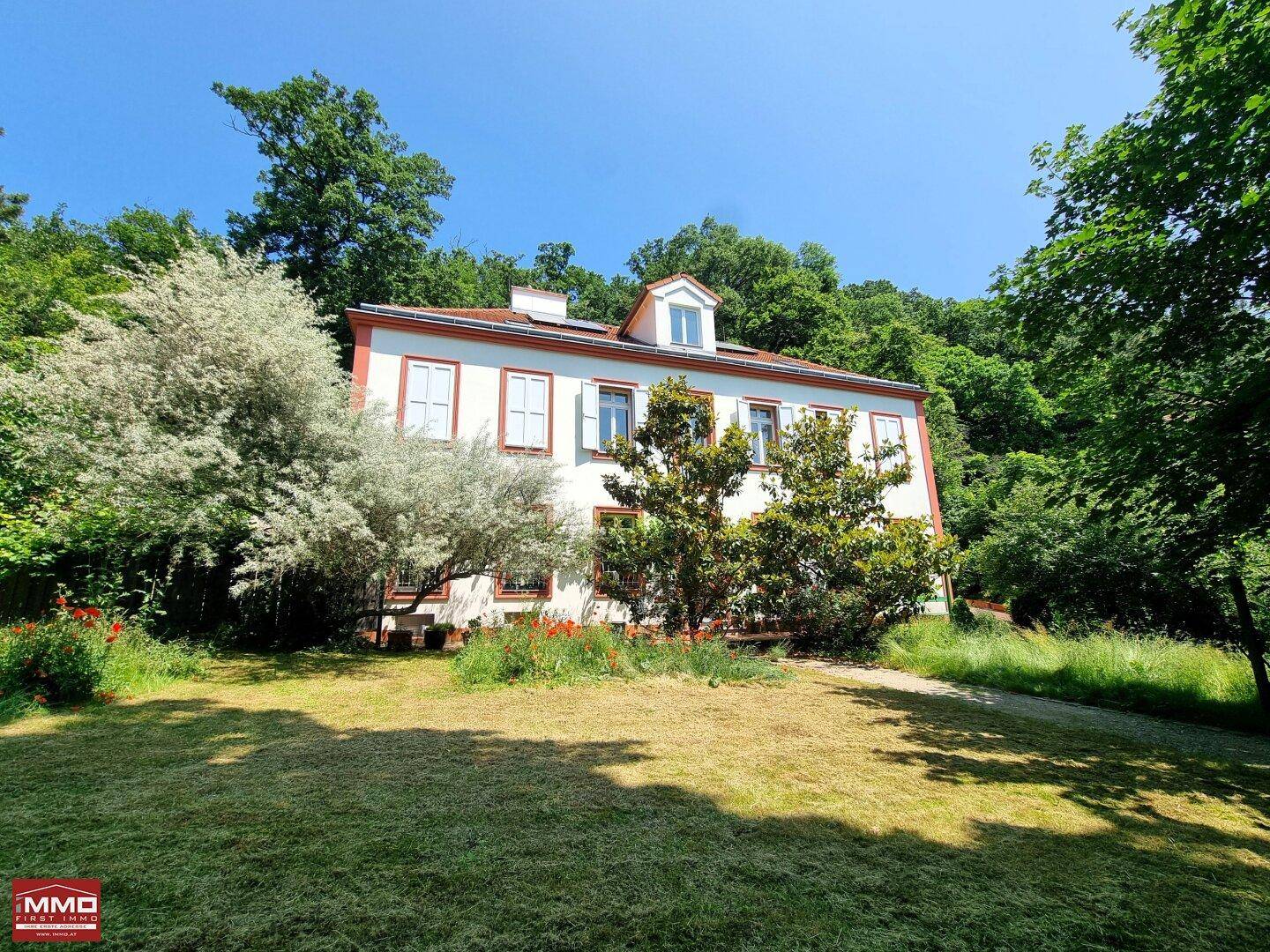 Weitläufiger Gartenbereich mit Rasenfläche und altem Baumbestand vor der eleganten Hausfassade.
