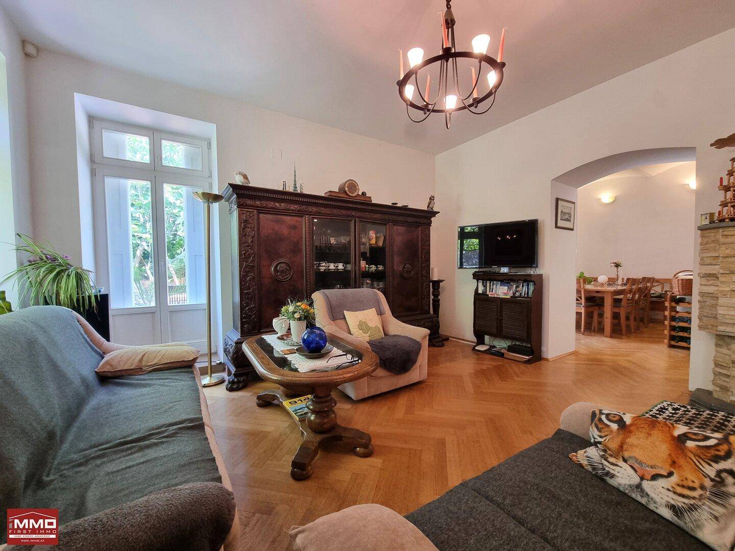 Gemütliches Wohnzimmer mit Fischgrätparkett, antiken Möbeln und Zugang zum Gartenbereich.