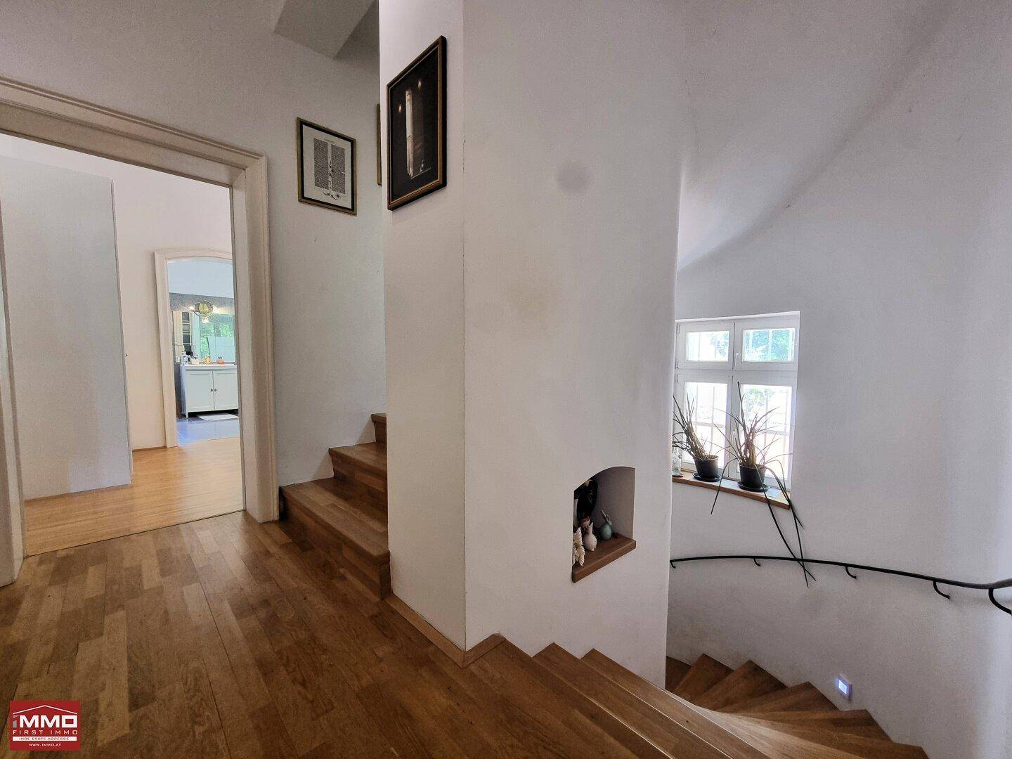 Heller Flur mit Holztreppe und Fenster, der zu weiteren Räumen im Obergeschoss führt.