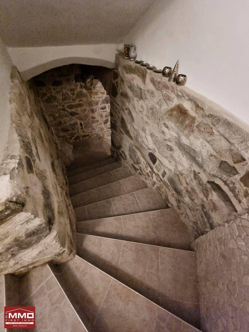 Rustikale Steintreppe führt hinunter in den Keller mit unverputzten Steinwänden und gefliestem Boden.