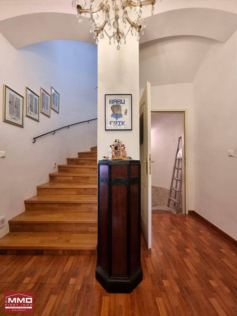 Eingangsbereich mit Holztreppe, elegantem Kronleuchter und dekorativer Säule, die den Raum gliedert.