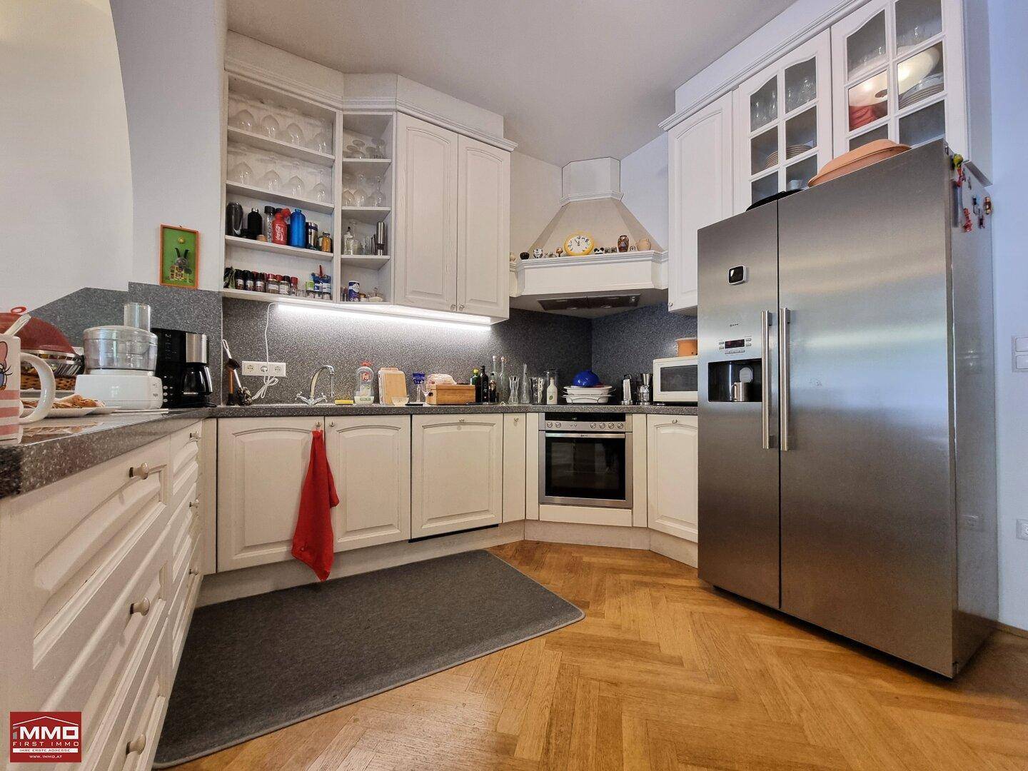 Moderne Küche mit weißen Schränken, Holzboden und großem Kühlschrank, ideal zum Kochen.