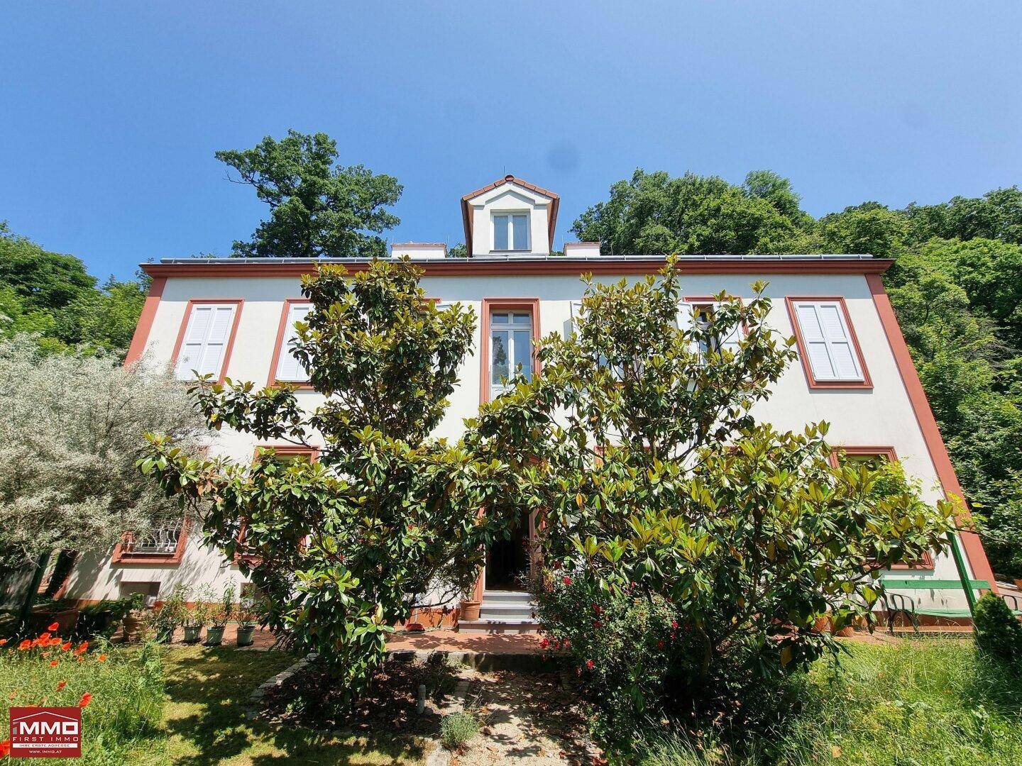 Ansicht der eleganten Hausfassade mit grünen Bäumen und Sträuchern im sonnigen Vorgarten.
