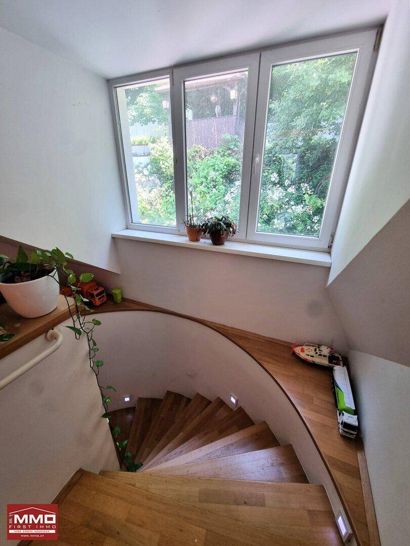 Holztreppe mit großen Fenstern, die einen grünen Ausblick in die Natur bieten und viel Licht hereinlassen.