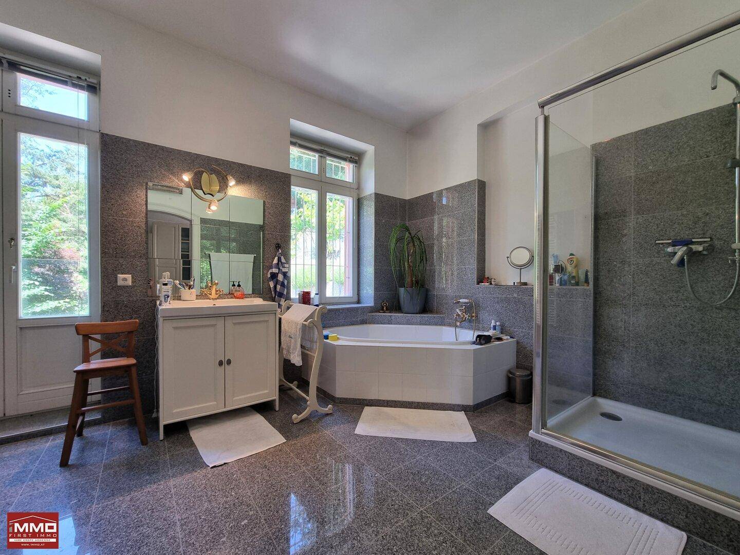 Geräumiges Badezimmer mit Eckbadewanne, separater Dusche und großformatigen grauen Fliesen.
