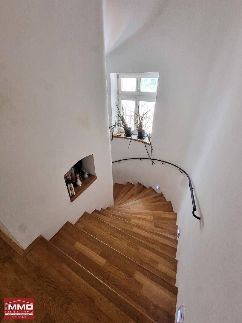 Elegante Wendeltreppe aus Holz mit Geländer und einem kleinen Fenster für natürliches Licht.