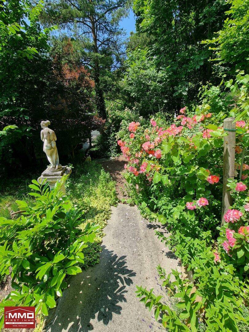 Romantischer Gartenweg mit einer klassischen Statue und blühenden Rosenbüschen.