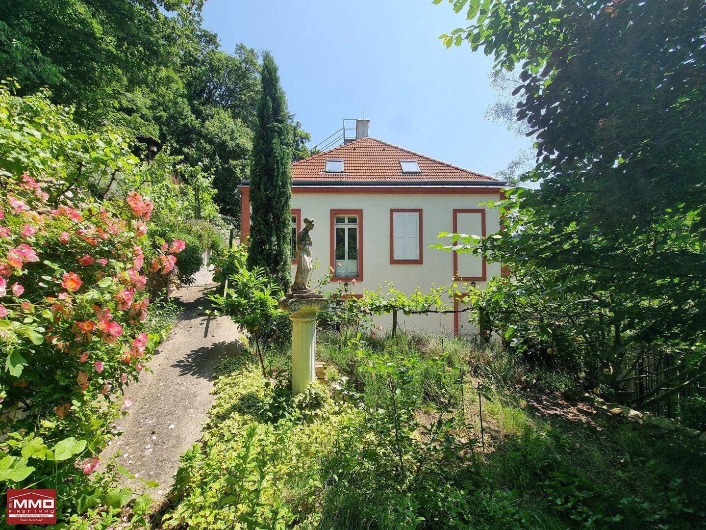Malerischer Garten mit Rosenbüschen, einer klassischen Statue und üppiger Vegetation.