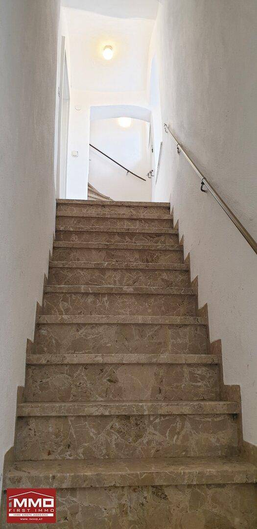 Historische Steintreppe in einem Altbau mit Handlauf, die nach oben führt.