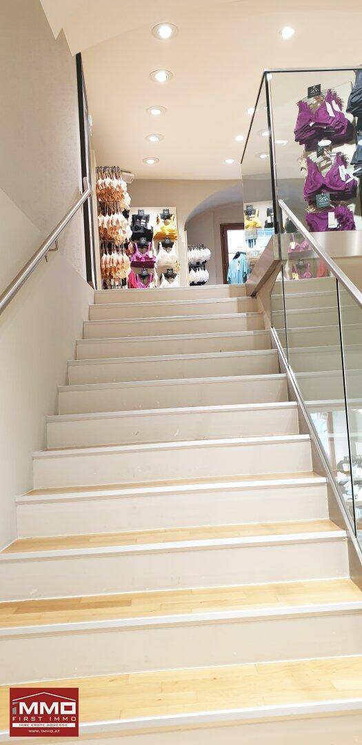 Helle Treppe mit Glasgeländer führt zu einer oberen Etage im modernen Verkaufsraum.