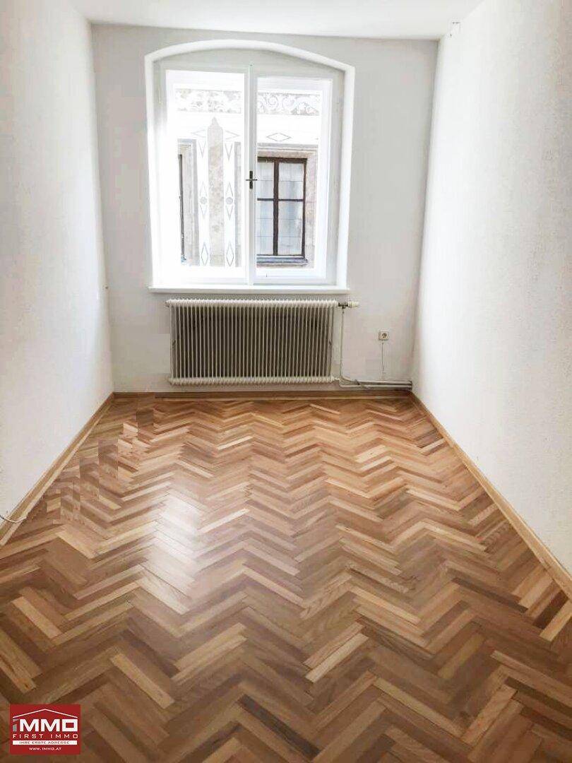 Kleiner, heller Raum mit Fischgrätparkett und einem Fenster, ideal als Schlafzimmer.