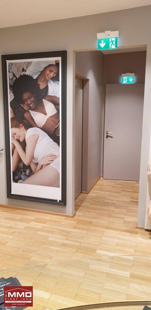 Heller Flur im Geschäft mit großem Werbebild und Notausgangsschildern.