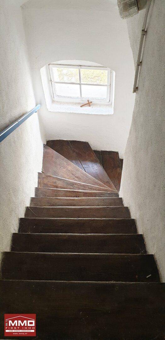 Rustikale Holztreppe mit kleinem Fenster im oberen Bereich, die nach oben führt.