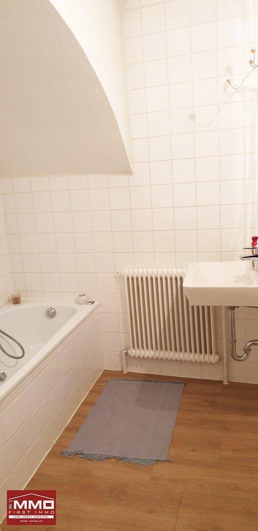 Helles Badezimmer mit Badewanne, Waschbecken und weißen Wandfliesen.