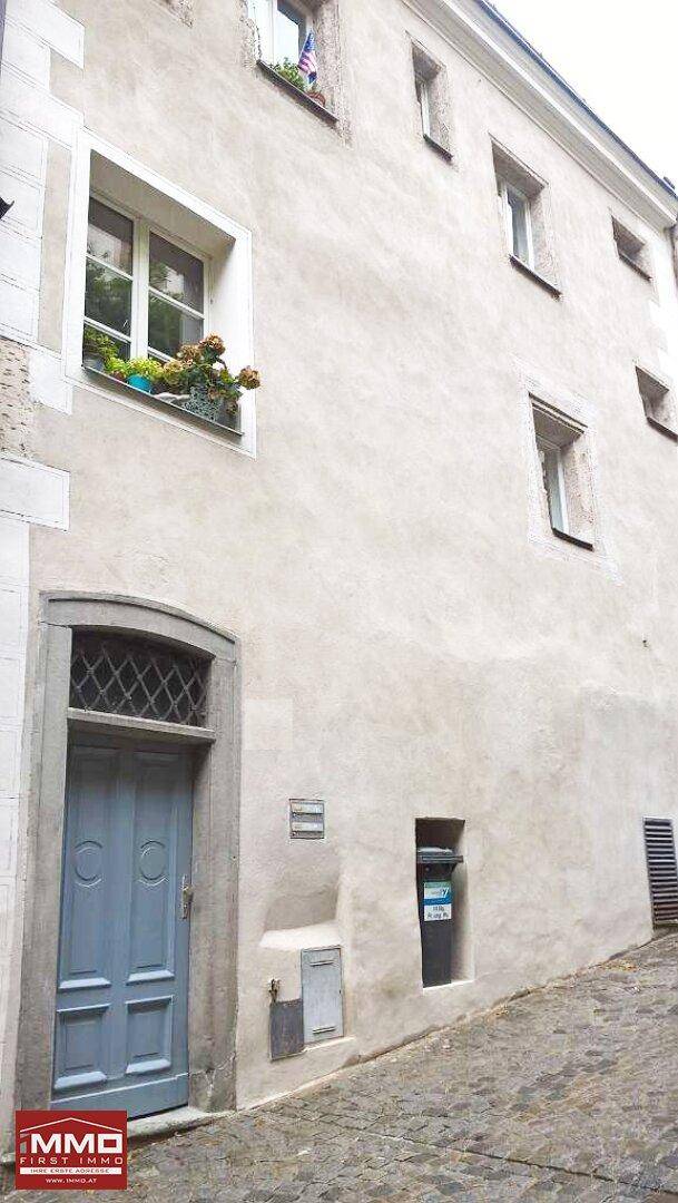 Historische Gebäudefassade mit heller Putzoberfläche, einer blauen Holztür und traditionellen Fenstern.