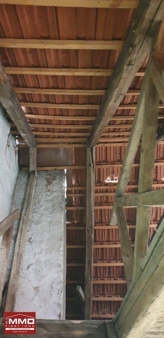 Blick in den Dachstuhl mit freiliegenden Holzbalken und der Unterseite der Dachziegel, zeigt die Rohbauweise.
