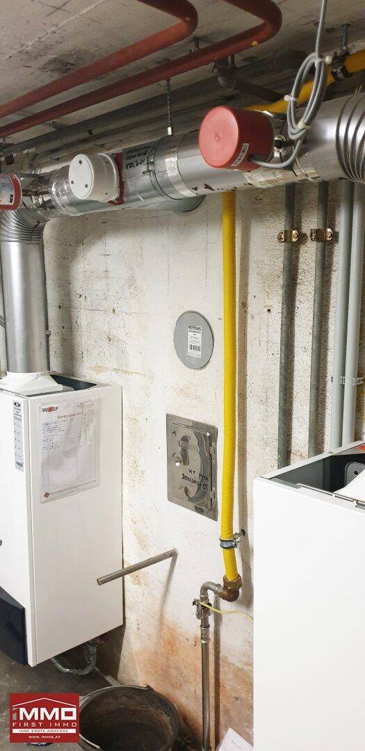 Heizungsraum mit komplexen Rohrleitungen, einem Warmwasserbereiter und gelben Gasleitungen an der Wand.