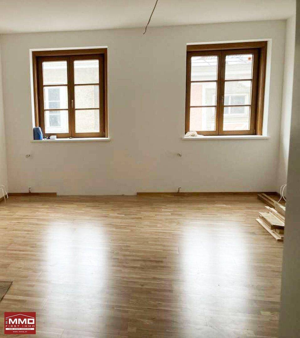 Heller, leerer Raum mit Holzplankenboden und zwei Fenstern.