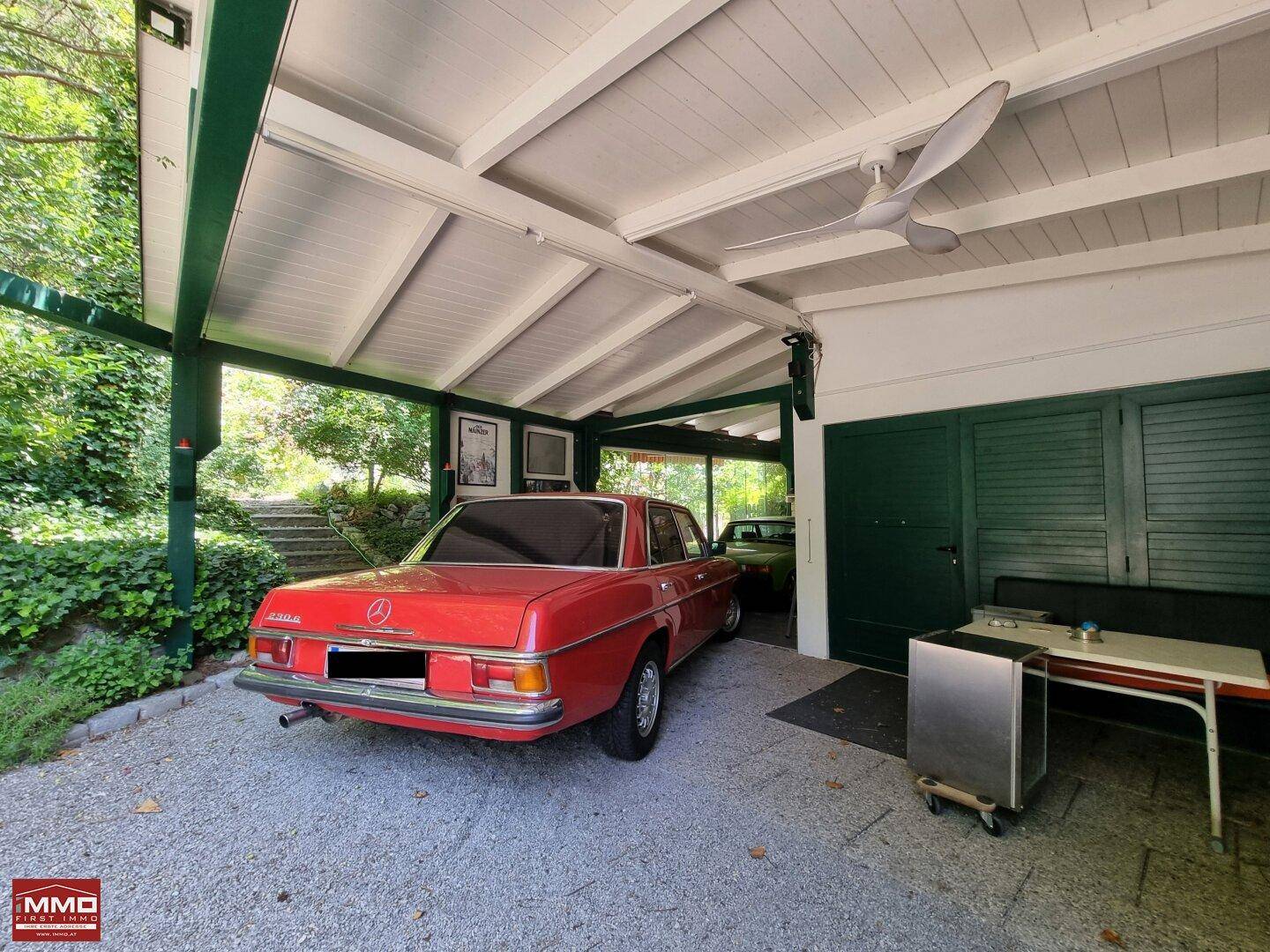 Geräumiger Carport mit einem roten Oldtimer und Deckenventilator für angenehme Temperaturen.
