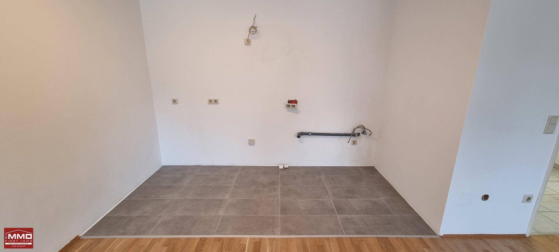 Vorbereiteter Küchenbereich mit Fliesenboden und Anschlüssen für die Kücheninstallation.