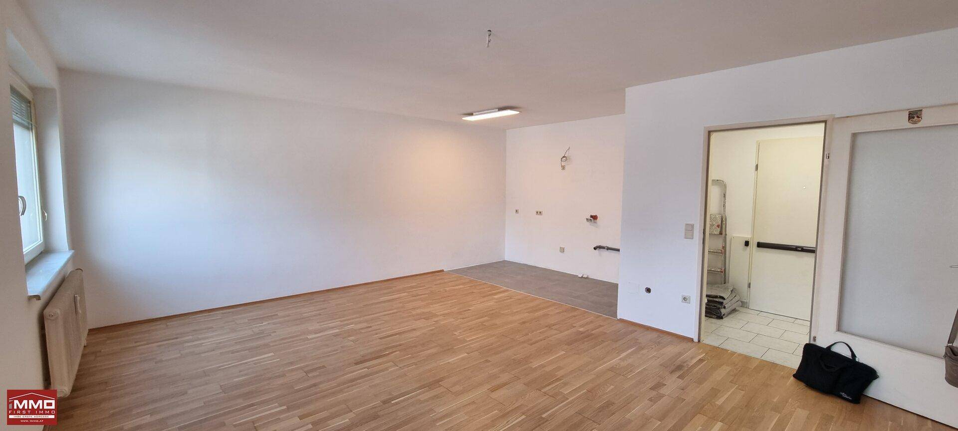 Geräumiger Wohnbereich mit Holzboden und vorbereitetem Bereich für eine offene Küche.
