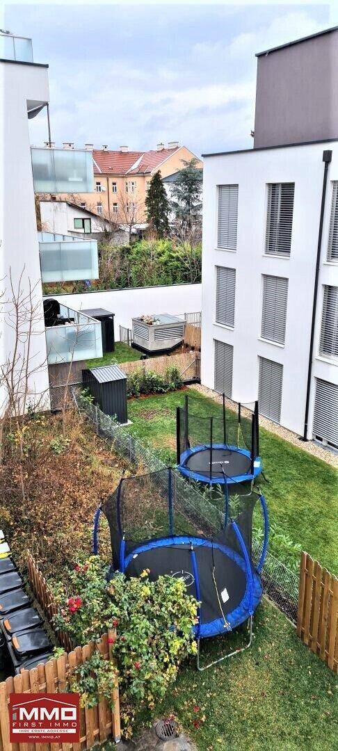 Gemeinschaftsgarten mit Trampolinen, Rasenflächen und Hecken zwischen modernen Gebäuden.