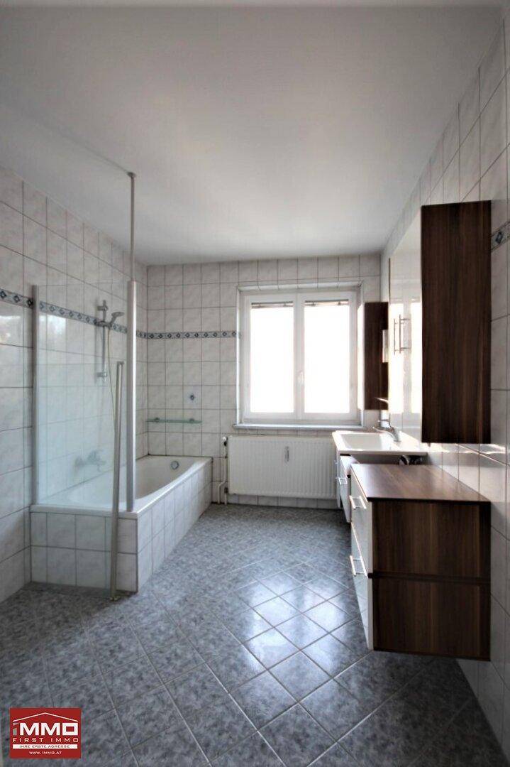 Badezimmer mit Badewanne, Duschmöglichkeit und hellen Fliesen, gut beleuchtet durch ein Fenster.