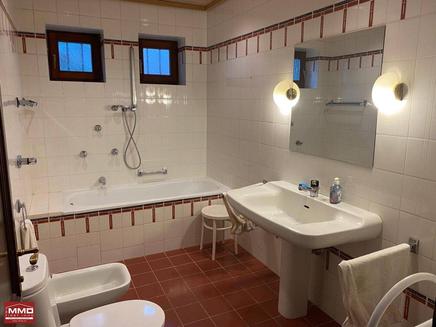 Helles Badezimmer im 80er-Jahre-Stil mit Badewanne, Bidet, Fenster und Fliesenboden.