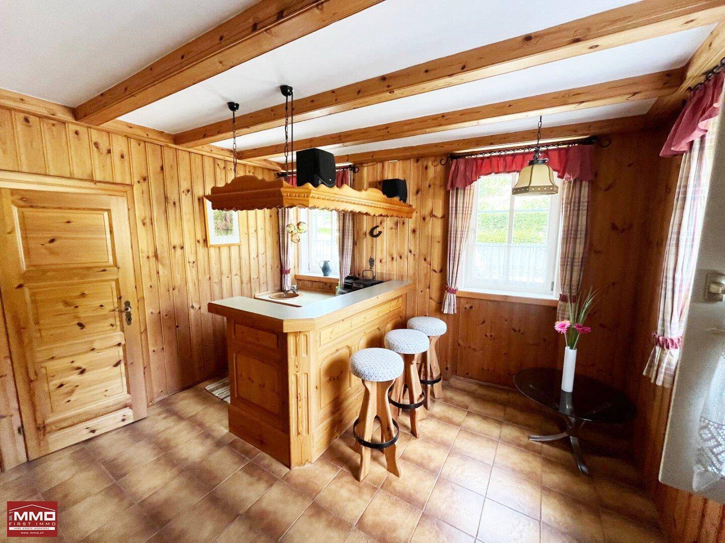 Traditionelle Bar mit Holzbalken, Holzvertäfelung und Hockern im Landhausstil.