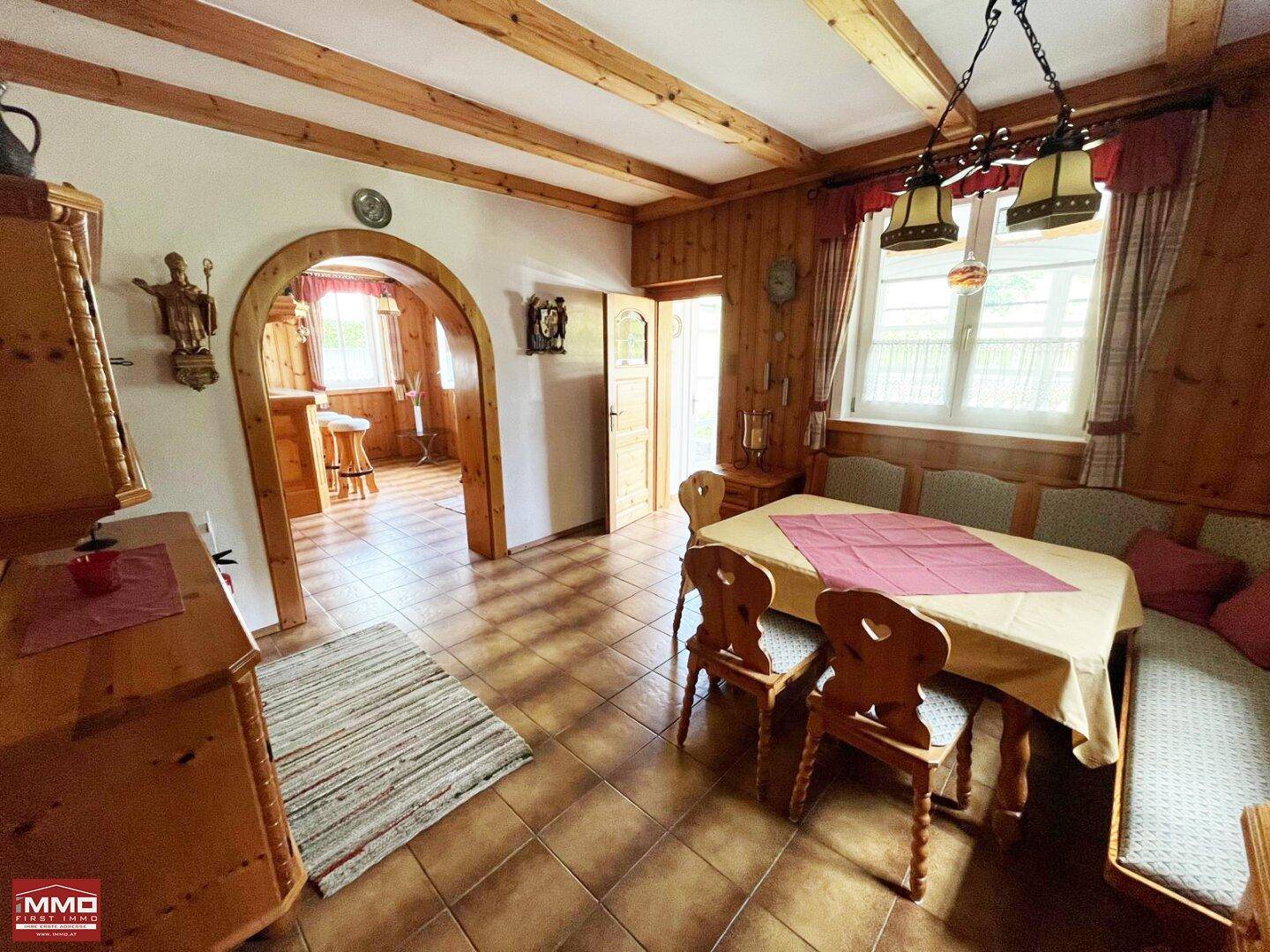 Traditioneller Essbereich mit Holzbalken, gefliestem Boden und Zugang zu einem weiteren Raum.