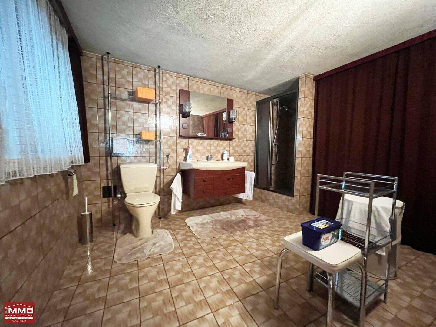 Geräumiges Badezimmer mit braunen Fliesen, Dusche und traditionellem Waschtisch.