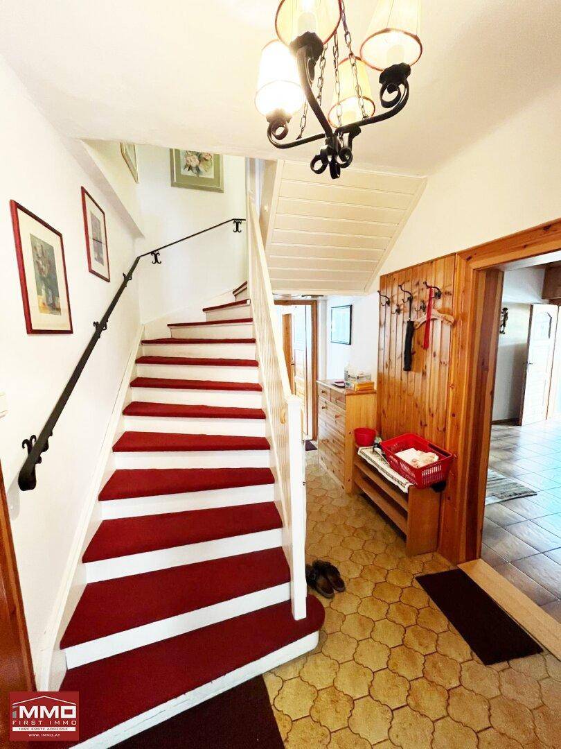 Eingangsbereich mit Holzvertäfelung, gefliestem Boden und einer Treppe mit rotem Teppich.