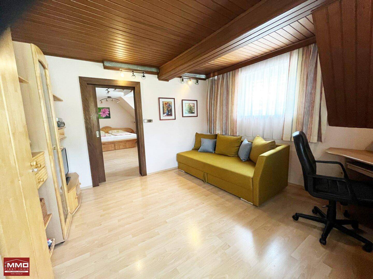 Helles Arbeitszimmer mit Holzboden, Holzbalkendecke und Zugang zu einem weiteren Schlafzimmer.