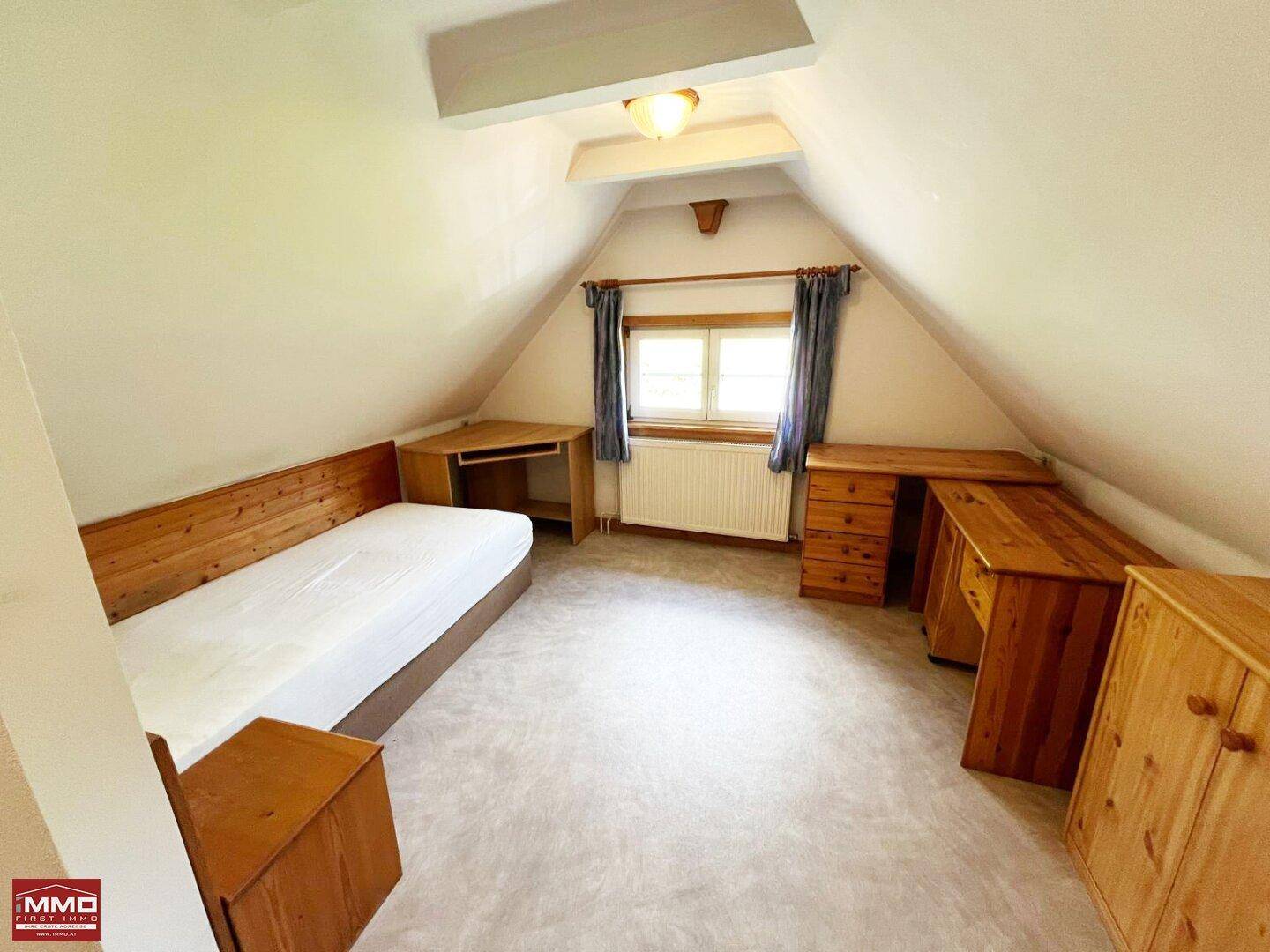 Helles Schlafzimmer im Dachgeschoss mit Teppichboden, Dachschrägen und Holzmöbeln.