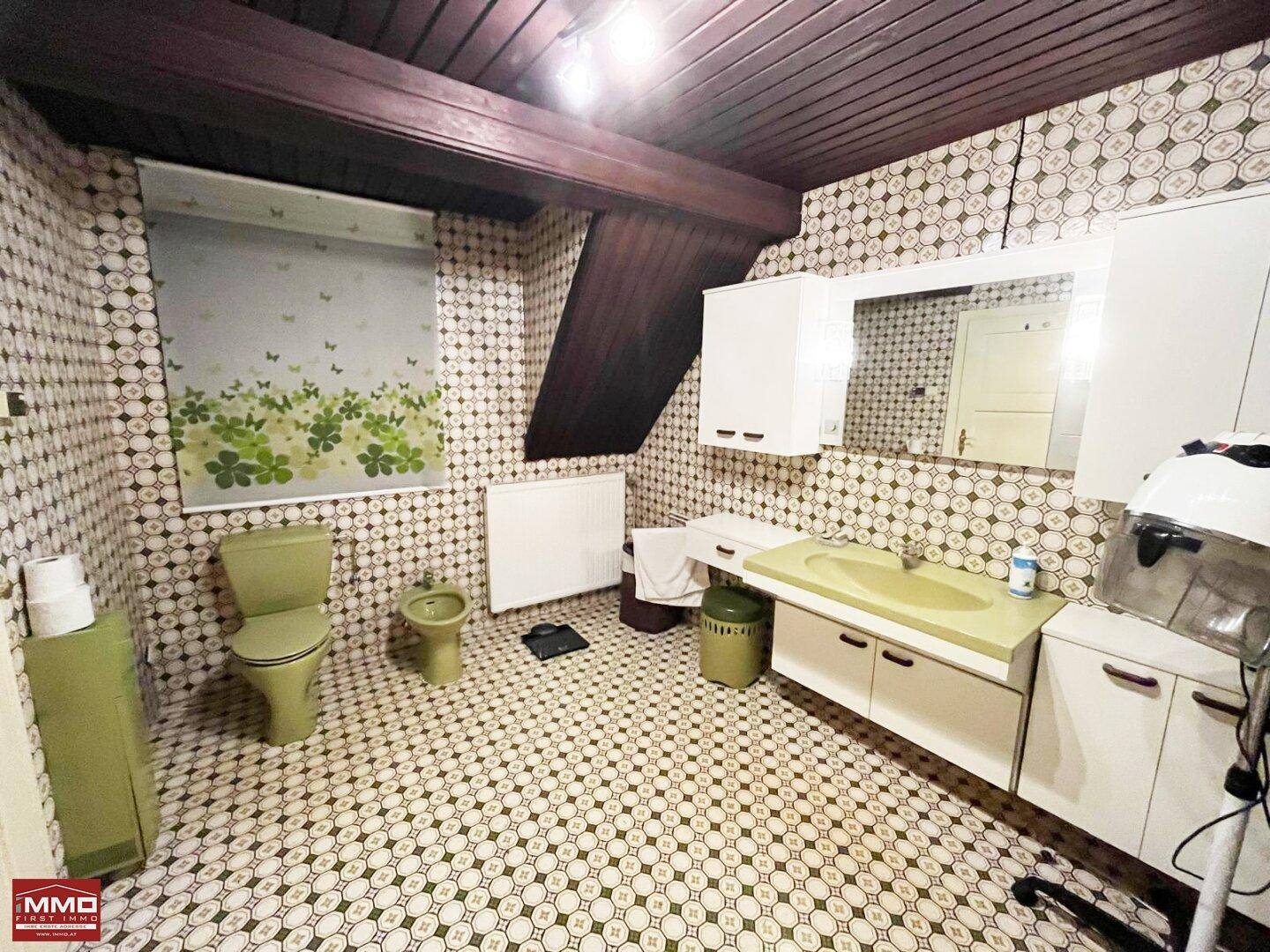 Badezimmer im 80er-Jahre-Stil mit gemusterten Fliesen, grüner Sanitärausstattung und Holzbalken.