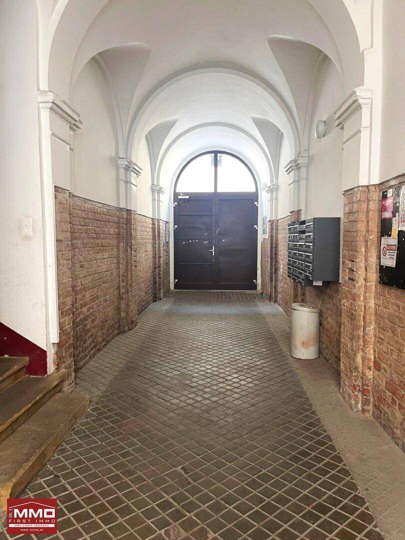 Historischer Hausflur mit Gewölbedecke, unverputzten Ziegelwänden und einem großen Tor am Ende.