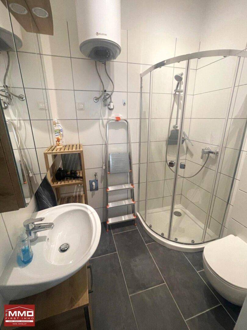 Modernes Badezimmer mit Eckdusche, WC, Waschbecken und einem Warmwasserboiler an der Wand.