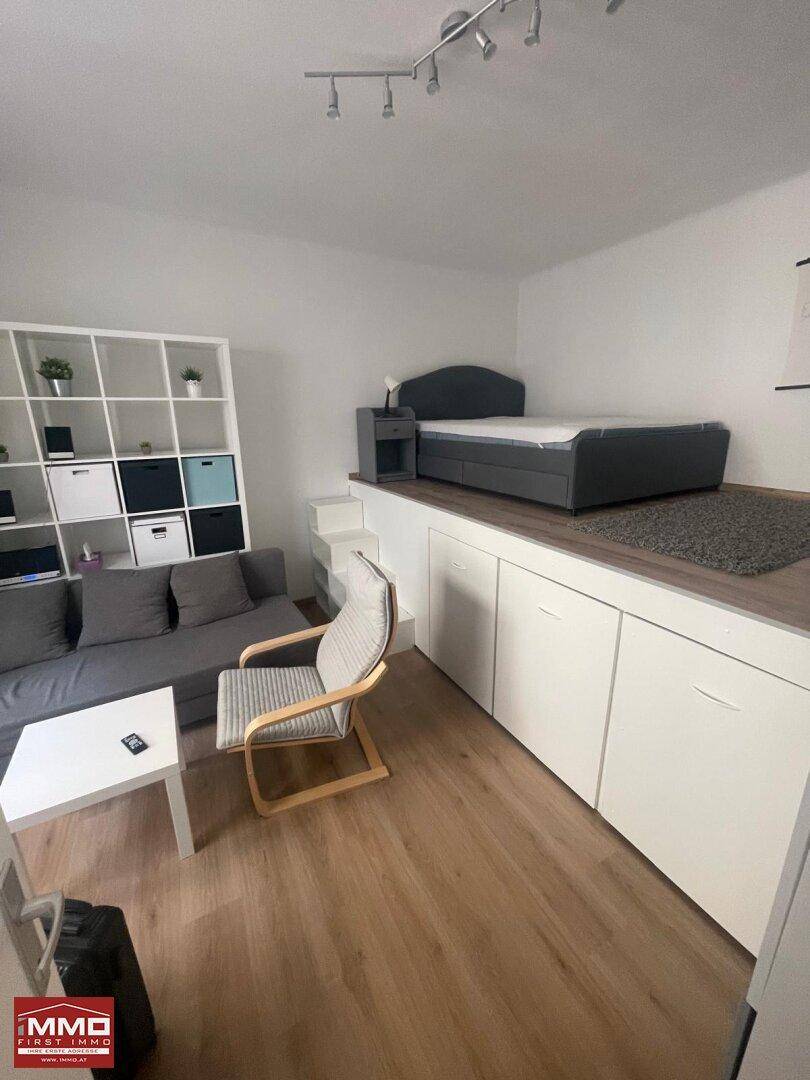 Kombinierter Wohn- und Schlafbereich mit erhöhtem Bett auf einer Plattform mit integriertem Stauraum.