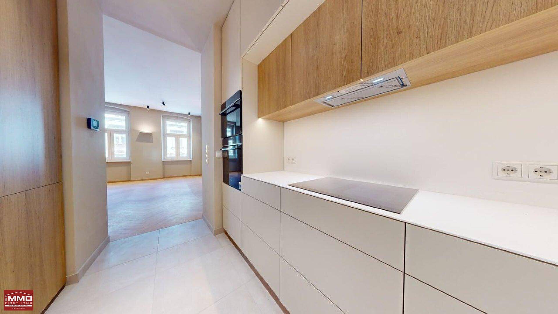 Helle Küche mit Induktionskochfeld, Dunstabzugshaube und Blick in den angrenzenden Wohnbereich.