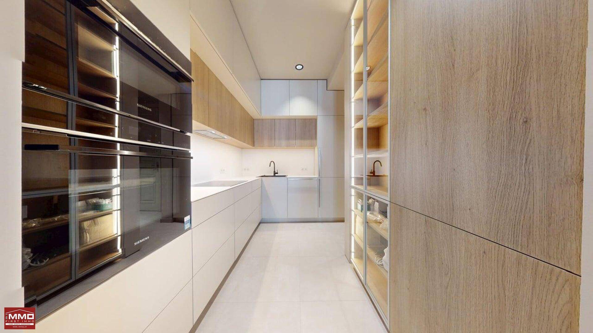 Moderne Küche mit integrierten Siemens-Geräten, hellen Holz- und weißen Schränken sowie Fliesenboden.