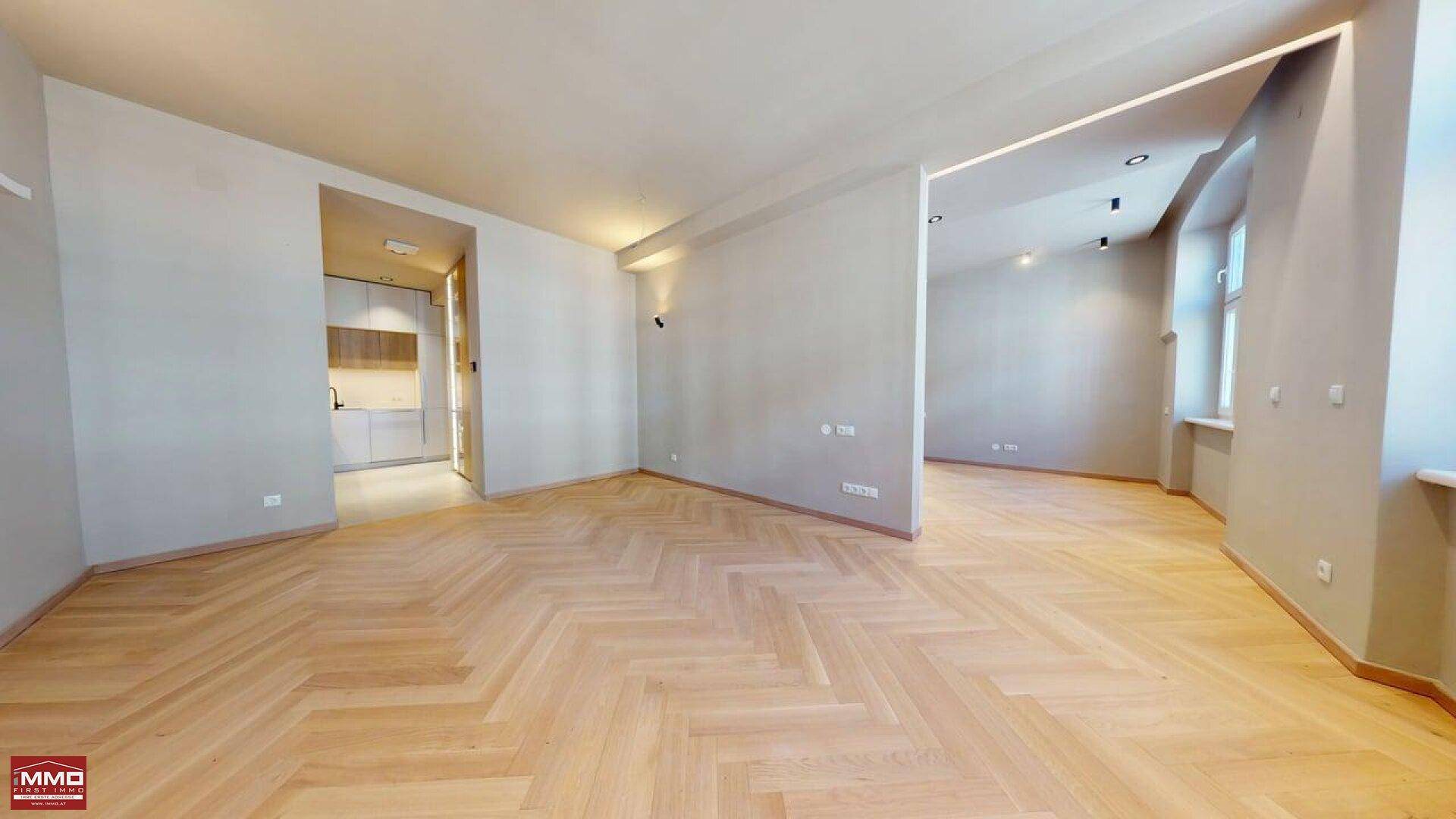 Geräumiges Wohnzimmer mit elegantem Fischgrätparkett und hellem Ambiente, offen zur Küche.