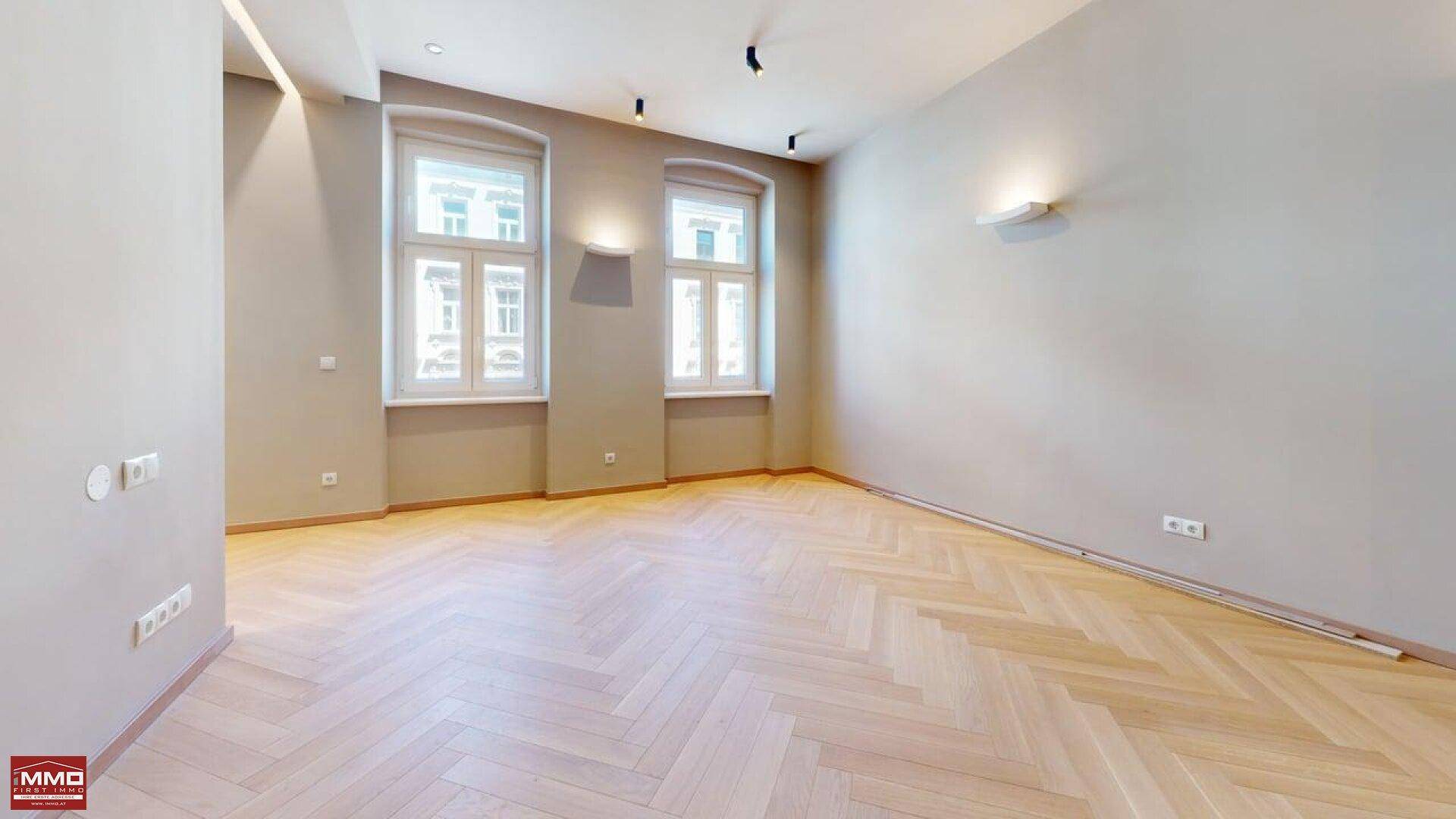 Lichtdurchflutetes Wohnzimmer mit klassischem Fischgrätparkett und zwei hohen Fenstern.