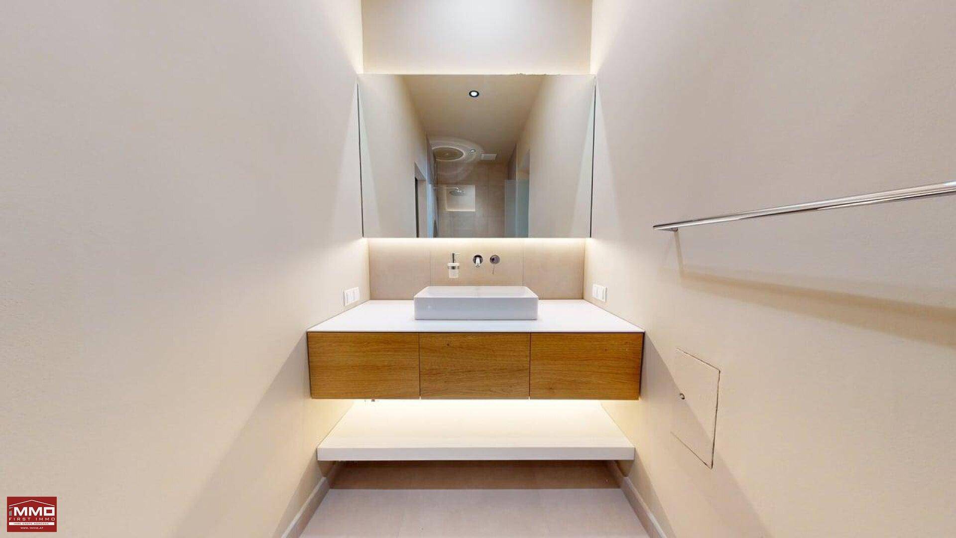 Elegantes Badezimmer mit schwebendem Waschtisch, integrierter Beleuchtung und großem Spiegel.