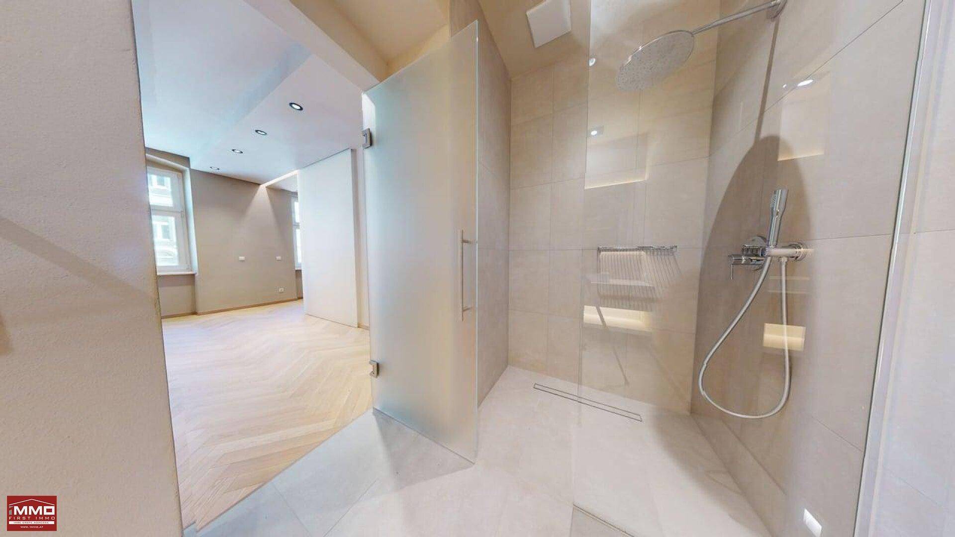 Helles Badezimmer mit begehbarer Regendusche, Glasabtrennung und Blick in den Wohnbereich.