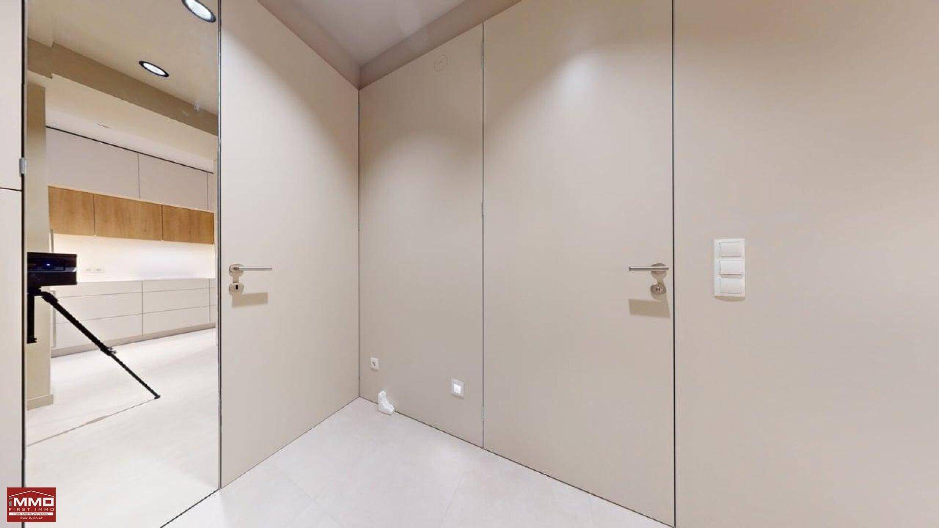 Ecke eines Raumes mit Fliesenboden und schlichten Wänden, die die Küche im Spiegel reflektieren.