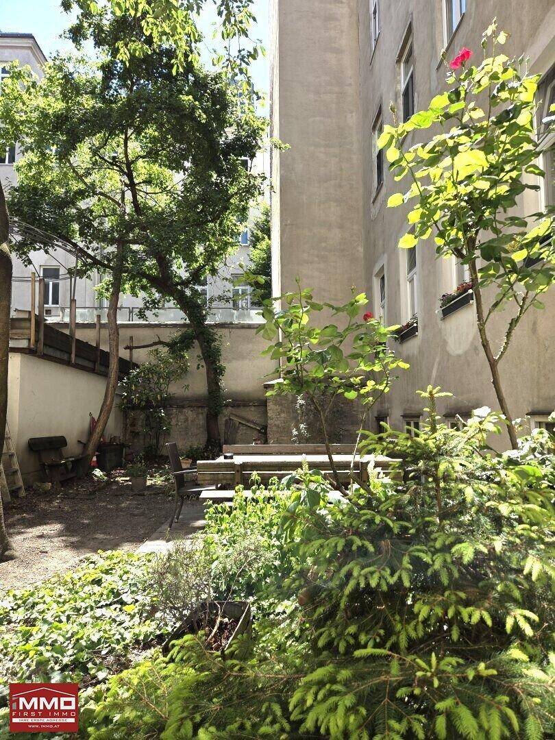 Grüner Innenhof mit Bäumen, Sitzgelegenheiten und üppiger Vegetation zwischen den Gebäuden.