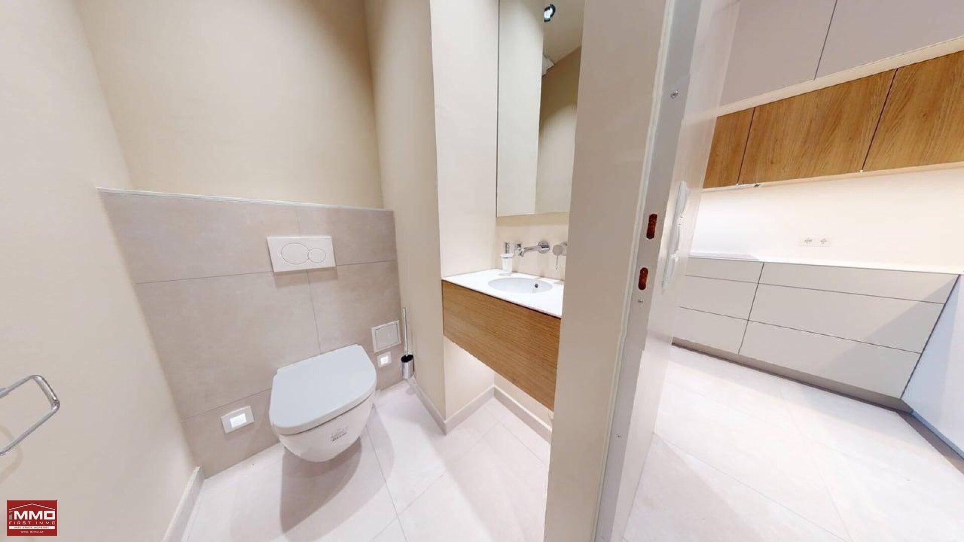 Helles Gäste-WC mit wandhängender Toilette, Waschtisch und Blick in die angrenzende Küche.