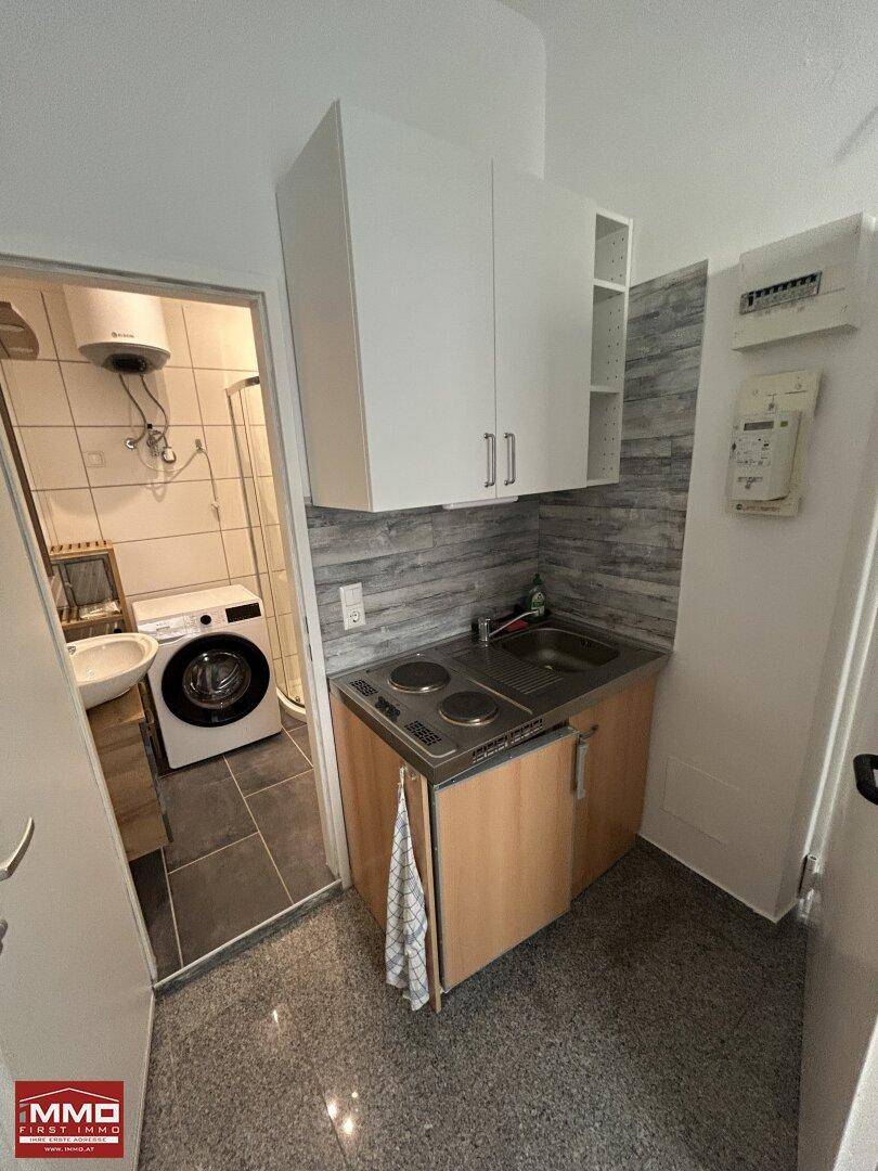 Funktionale Küchenzeile mit Kochfeld und Spüle, daneben ein Badezimmer mit Waschmaschine.